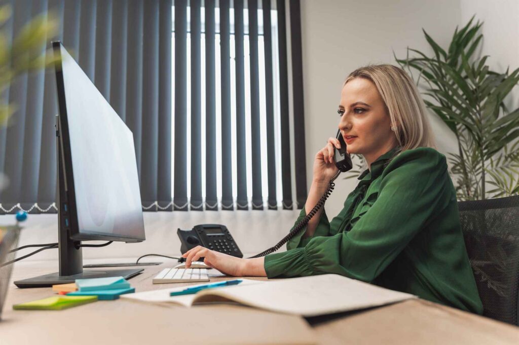 a woman in a green blouse is sitting at a desk ta       utc x